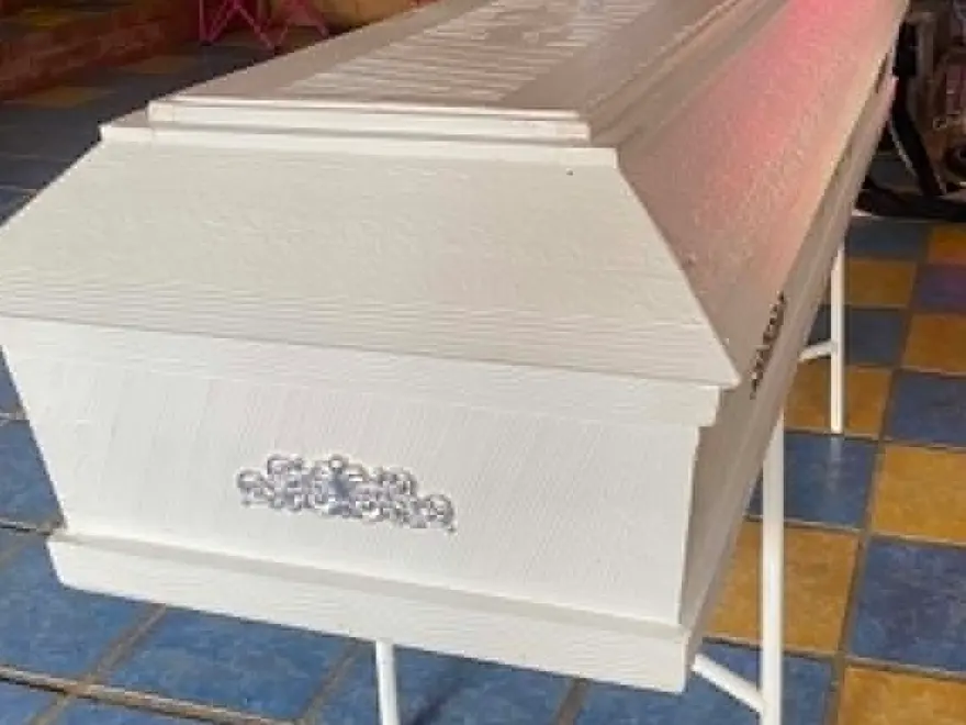 A sample plain white casket with silver ornaments, closed on its bier