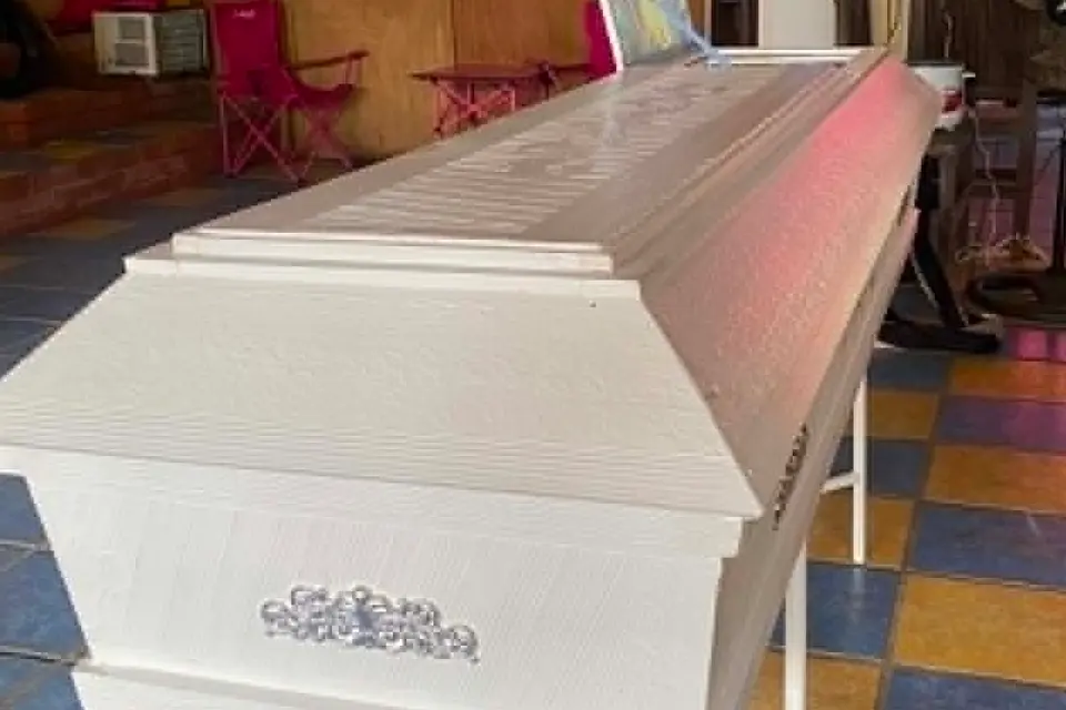 Illustrative sample coffin — A plain white casket with silver ornaments, photographed closed on its bier