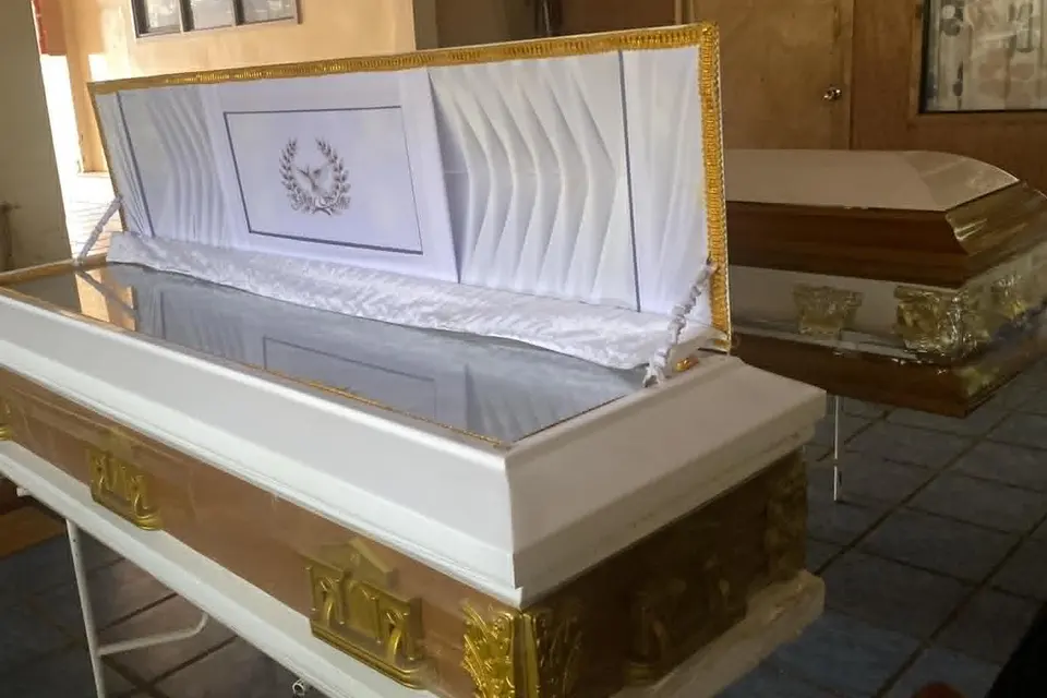 Illustrative sample coffin — A white casket with gold trim and a raised full-glass lid, its white interior carrying a laurel wreath emblem