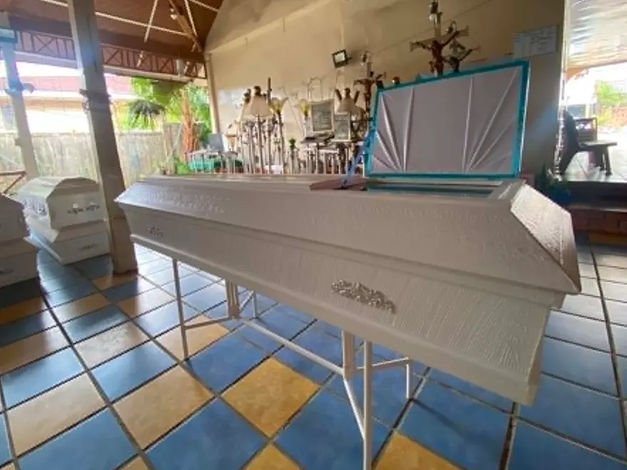 A casket resting on a bier in the office's own hall, its lid raised — the office's care before a viewing