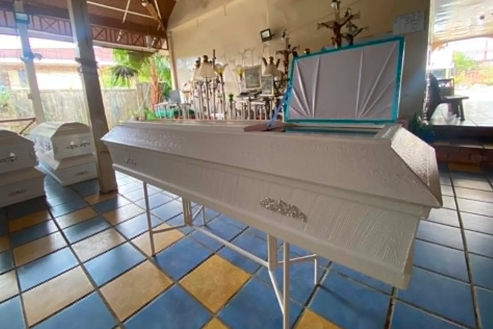 Illustrative sample coffin — A plain white casket with silver ornaments and its lid raised on a bier, in a chapel hall with other caskets behind