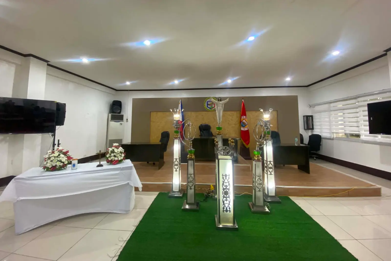 The chapel hall in the client's own photograph — a draped side table and tall candle pedestals on a green carpet