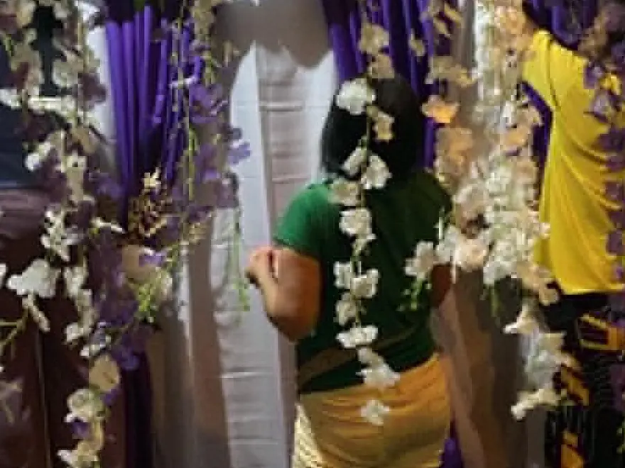 Two staff members seen from behind, hanging white flower sprays and arranging purple drapes over a white backdrop