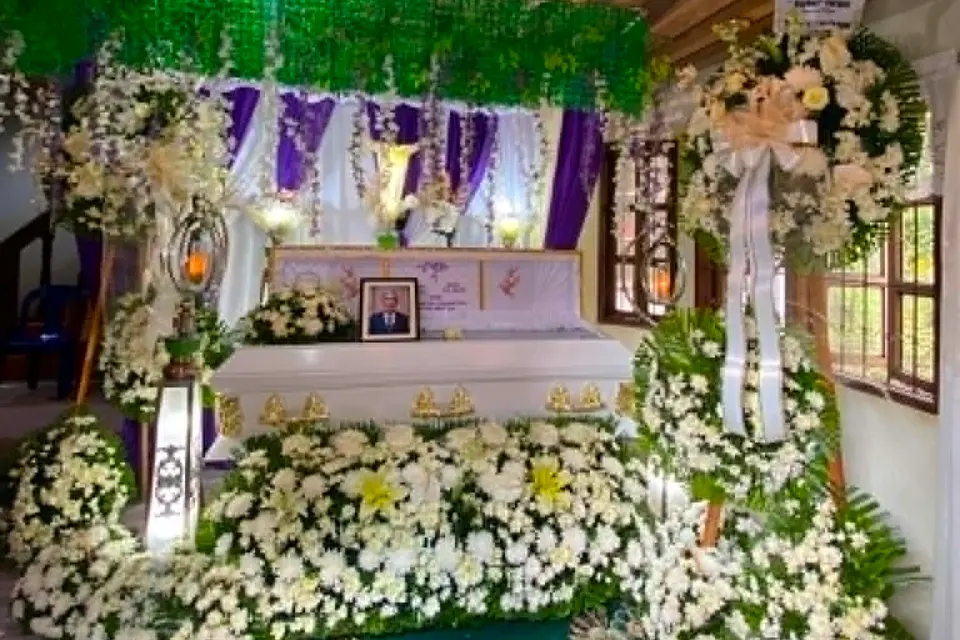 A finished wake set-up — a white casket banked in white flowers under purple drapes the office prepared